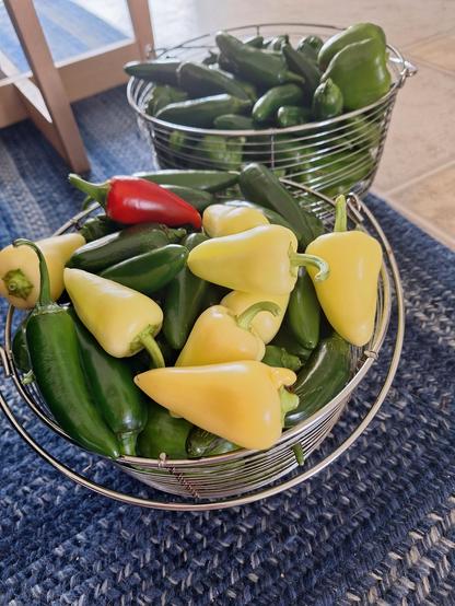 Two wire baskets overflowing with jalapenos, Italian frying peppers, small green bell peppers, and a few red or yellow Santa Fe chiles.