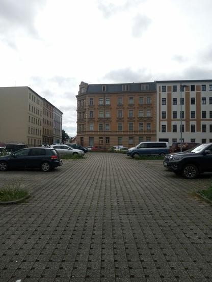 Ein Parkplatz aus Rasenpflastersteinen, ohne Rasen in den Pflastersteinen. Kleine Grünstreifen. Autos.