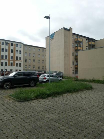 Ein Parkplatz aus Rasenpflastersteinen, ohne Rasen in den Pflastersteinen. Kleine Grünstreifen. Autos.