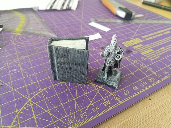 A finished, tiny, cased book. Covered in grey book cloth, and slightly smaller than the 28mm tabletop necromancer next to it. (Who admittedly has both a tall hat and a base, so a slightly unfair comparison.)