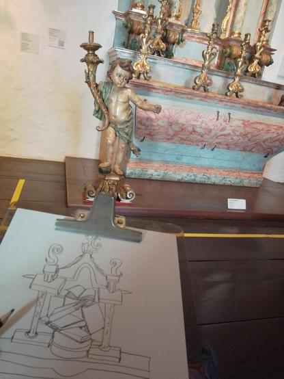 na foto um detalhe de altar em tons azuis e rosado e ao lado esquerdo uma prancheta com a reprodução do mesmo