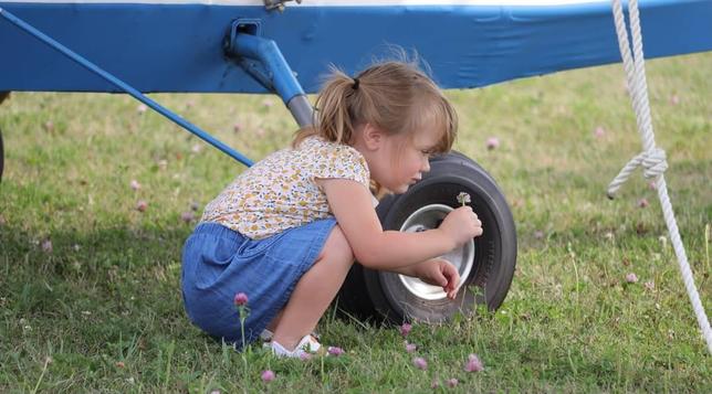 A young girl picking flowers next to the wheel of a small aircraft.