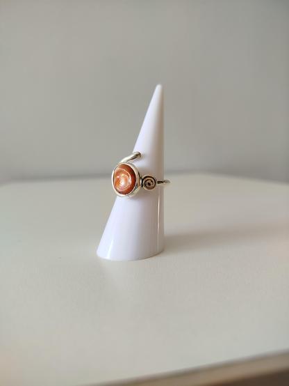 A silver ring with an orange gemstone. it's placed on white cone