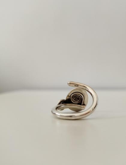 The back of an open end silver ring. it has a spiral motif
