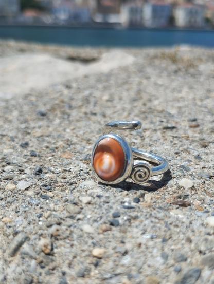 A silver ring with an orange gemstone on grey sand
