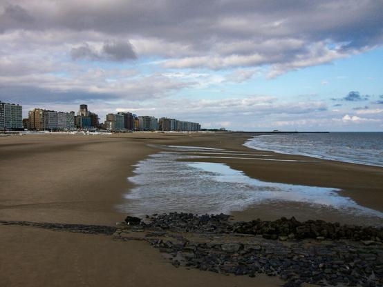 Color photo of an empty beach. In the background, a row of modern apartment buildings dominate the skyline.