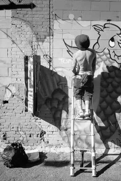 A graffiti artist stands on a ladder and contemplates his next moves.