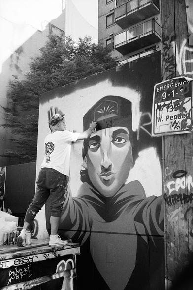 A man adds some finishing touches to piece from atop a dumpster.