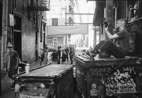 A photographer captures a scene in a dark alley as pedestrians mill about.