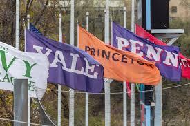 The image features a row of flags on flagpoles, each representing a different institution. From left to right, the flags are white with green text, purple with white text reading "YALE," orange with black text reading "PRINCETON," and purple with white text reading "PENN." The flags are waving in the wind, suggesting a breezy day. The background includes trees and a building, indicating an outdoor setting. The flags are mounted on metal flagpoles, and the scene is well-lit, likely during the daytime.

Provided by @altbot, generated privately and locally using Ovis2-8B