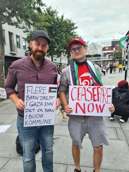 To folk står på palestina-demo i Bodø. De holder en plakat hver. På den ene står det "Flere barn drept i Gaza enn det er barn i Bodø Kommune". På den andre står det "Ceasefire Now"
