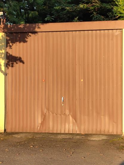 ein Garagentor mit einem senkrechten Griff in der Mitte, darüber zwei Reflektoren als Augen. darunter eine Einbeulung mit senkrechten Mundfalten