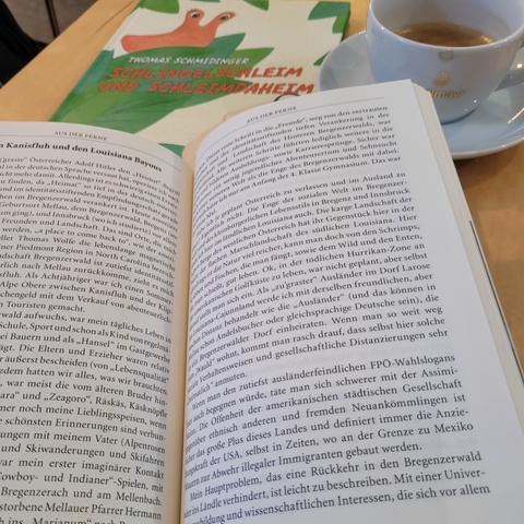 Aufgeschlagenes Buch, dahinter Bilderbuch und Tasse Kaffee