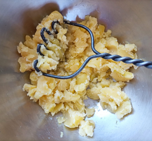 In einer Schüssel die mit einem Kartoffelstampfer grob zerdrückten Kartoffeln.