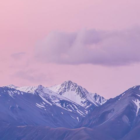 Snow-capped mountain peak in Fiordland National Park, New Zealand, seen under a pink and purple sky. The rugged terrain is surrounded by alpine ridges and dramatic light, evoking the remote beauty of the South Island.