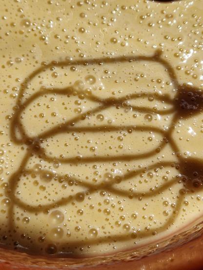 close-up of pancake batter, sunlight shining on the little bubbles on the surface, with the shadow lines of the mixer beaters as a contrasting shape