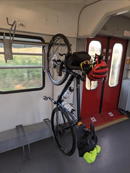 Na wieszaku w pociągu wisi rower, a z jego kierownicy zwisa czerwony kask.