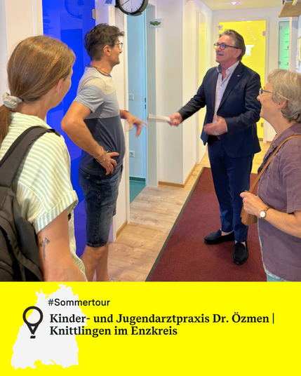Vier Personen stehen im Flur einer Kinder- und Jugendarztpraxis in Knittlingen. Minister Manne Lucha spricht, die anderen hören zu. Text: Sommertour. Kinder- und Jugendarztpraxis Dr. Özmen | 
Knittlingen im Enzkreis.