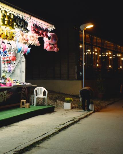 A shooting stand with lots of plush animals hanging around. A plastic chair at the front. The intense light of the stands covers the scene. The front panel says "good shot"