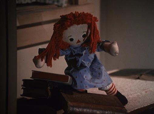 Raggedy Ann doll climbing on a desk with books.