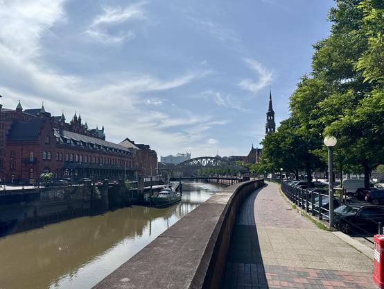 Dark red brick buildings at a canal at the Speicherstadt. A boat and a bridge in the background.