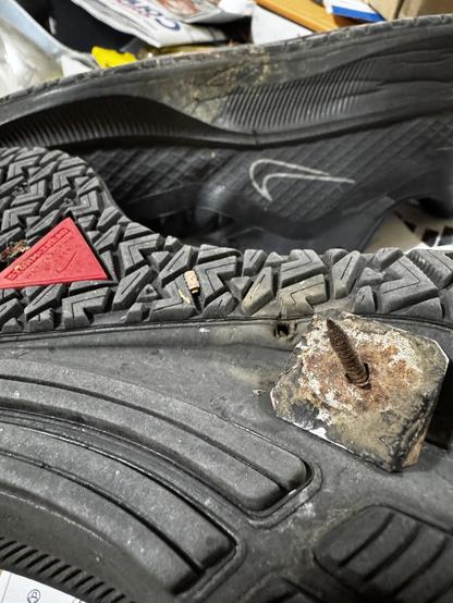 A roofing nail pulled out of a Nike tennis shoe sole with the penetrating hole visible.