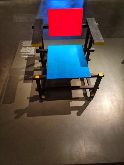 His often replicated slat chair design from 1929. It features a square light blue, almost cerulean, seat and a red square back, supported by rectangular black legs.