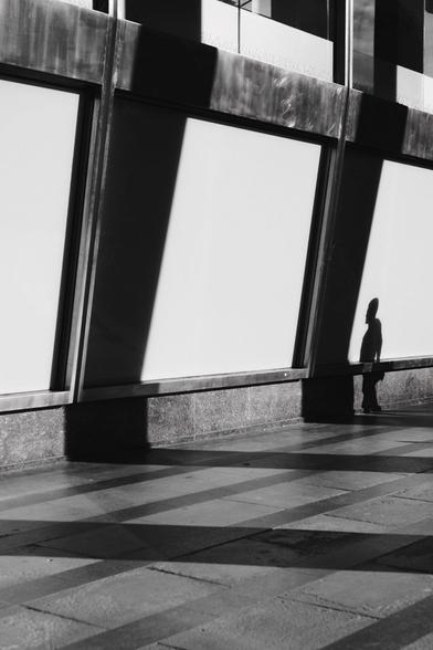 Blank shop windows are brightly lit but sunlight coming from the right. Shadows of columns are projected almost perfectly in between the windows as the shadow of a man is clearly visible in the last window.