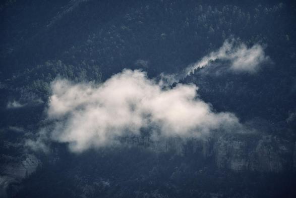 Low clouds drift across a dark, forested mountainside, partially veiling cliffs and trees.