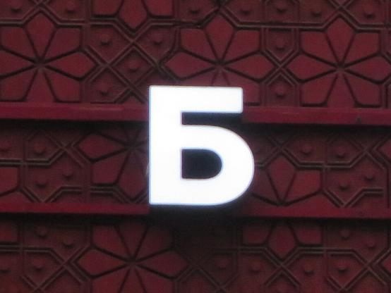 Белая буква Б на тёмно-красном орнаментальном фасаде ресторана. // A white B on the dark red ornamental facade of a restaurant.
