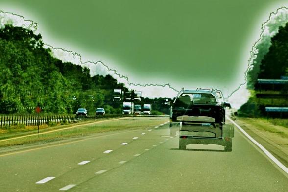 A surreal double exposure of a tree lined double highway is in a green toned retro-colour. A pick-up has a ghostly overlay, as does the highway lines, oncoming traffic on the other side of the divide, and trees.