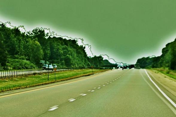 A surreal double exposure of a tree lined double highway is in a green toned retro-colour. Vehicles in the distance have a ghostly overlay, as does the highway lines, oncoming traffic on the other side of the divide, and trees.