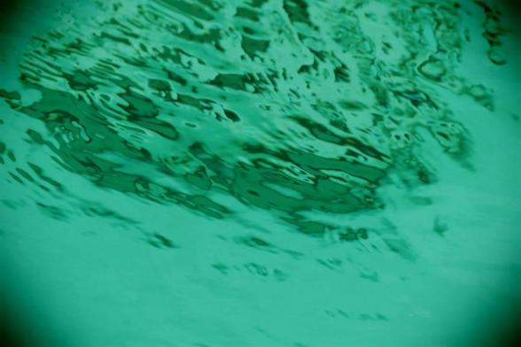 A surreal, dreamy close-up of ripples on the surface of the water in a swimming pool is in a green toned retro-colour.