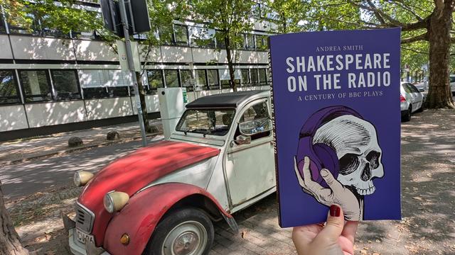 Holding the book "Shakespeare on the Radio" next to a red and white vintage car