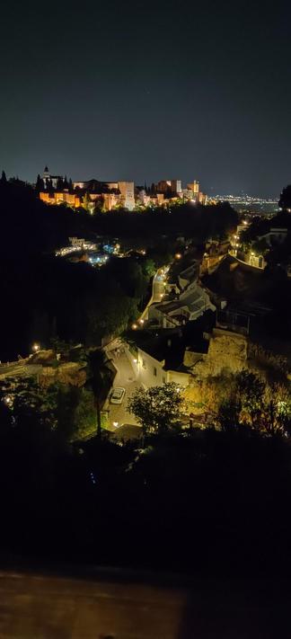Vista nocturna de la Alhambra iluminada desde el museo de las Cuevas del Sacromonte. En primer plano se puede ver parte del barrio del Sacromonte, con sus calles sinuosas iluminadas.