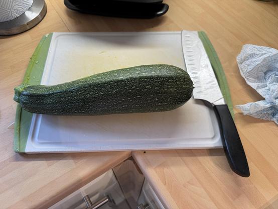 A very large courgette on a chopping board next to a chopping knife