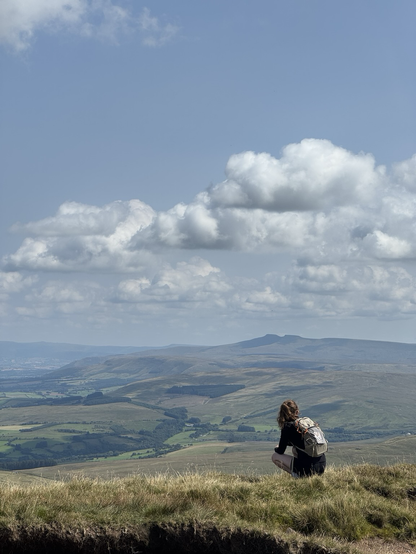 My daughter crouches like Batman on the edge of the grassy summit, surveying the Brecon Beacons laid out in front of her.