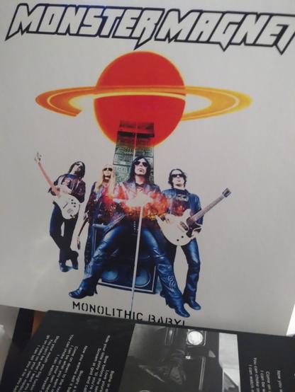 vinyl cover monster magnet - Monolhic baby 
photo des membres du groupe sur une fond blanc les musiciens s'opposant sur un combo d'ampli, une planète rouge style Jupiter  tro'at au dessus d'eux