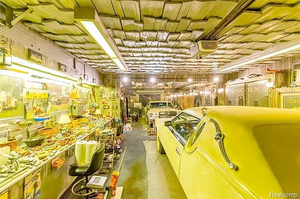 The interior of a garage with bright yellow shingled ceiling, and a bright yellow gigantic coupe in front of a mirrored wall. There is a long table going the length of the garage which is also bright yellow, covered in various tools and things.