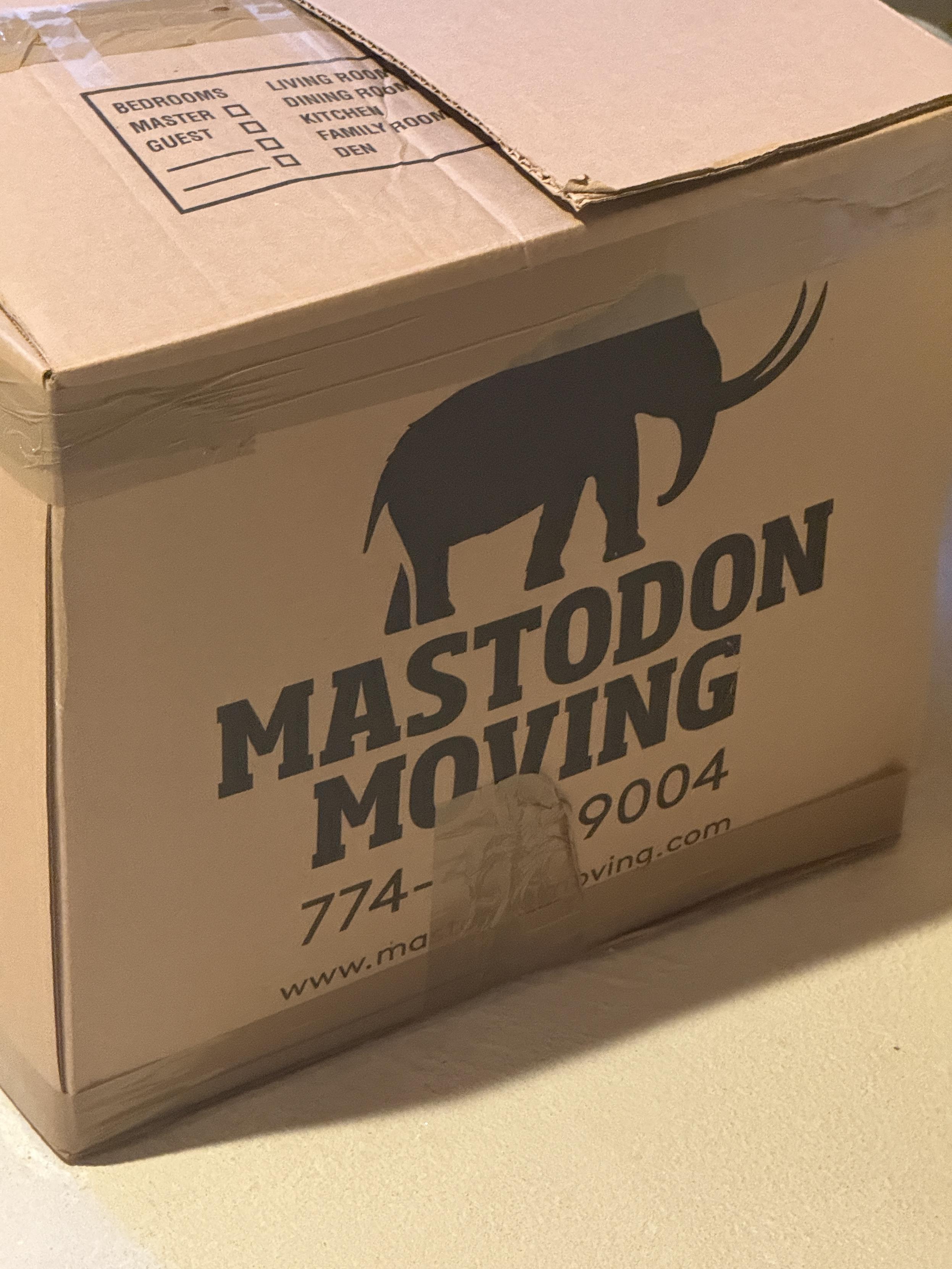 A photo of a cardboard moving box with a silhouette of a mastodon and the text "MASTODON MOVING" printed on it