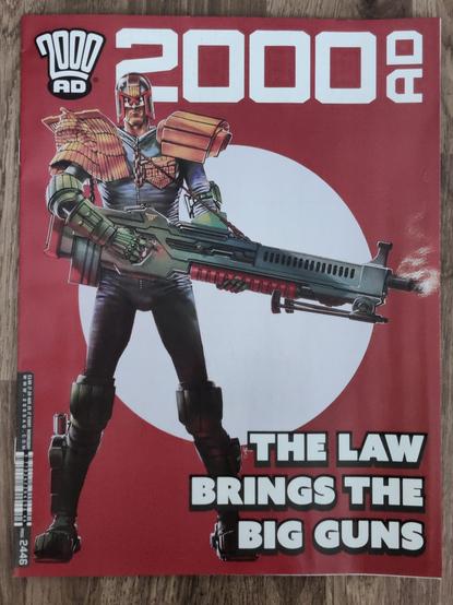 the cover to 2000AD prog 2446 featuring Judge Dredd holding a very big gun