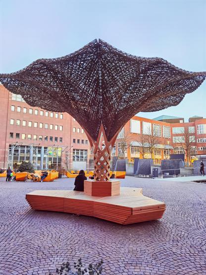Mobile Sitzgelegenheit mit integriertem, einer Baumkrone nachempfundenen Holzgeflecht, das Schatten spendet.
