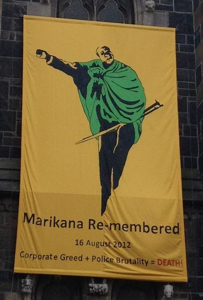 A commemorative banner outside the Central Methodist Mission in Cape Town's Green Market Square. Depicts a man in a green cape. Below him it reads: “Marikana Remembered. Corporate greed plus police brutality = DEATH!” By Discott - Own work, CC BY-SA 4.0, https://commons.wikimedia.org/w/index.php?curid=114052114