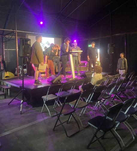 Een groepje mensen op een podium. Gekleurde lampen en alle stoelen nog leeg.