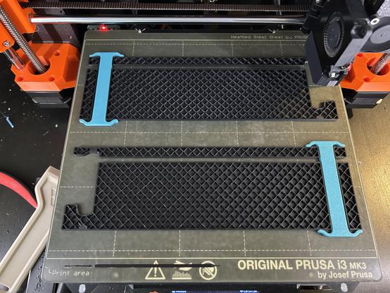 Two large 3D printed PLA parts are on the printer bed, partially printed.  Each has a 13mm wide channel with a PETG support block inserted.  The support block has serif-like wings at each end that press firmly against the PLA.