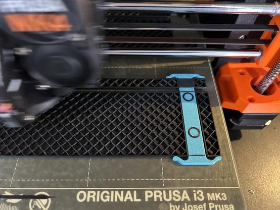 The printer is in the process of depositing the next layer of PLA onto a PETG support block.  On the support, there are two holes' perimeters, not attached to any other PLA , and elsewhere there are bridges across the blocks.  The print head is moving so fast it is a blur.
