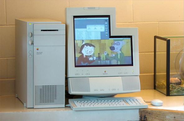 A photo of a macintosh Quadra 950 and Applevision display on a desk, with a keyboard, a mouse, and an organic mouse. The Applevision display is in an L shape, with the upper right corner missing. Onscreen is a Finder desktop, and a quicktime video playing in the bottom half.