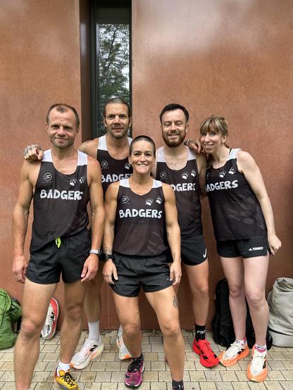 Three men and two women are wearing identical running outfits. They are probably members of a sports club. Their tank tops have ‘Badgers’ written on them. There is an atmosphere of genuine camaraderie.