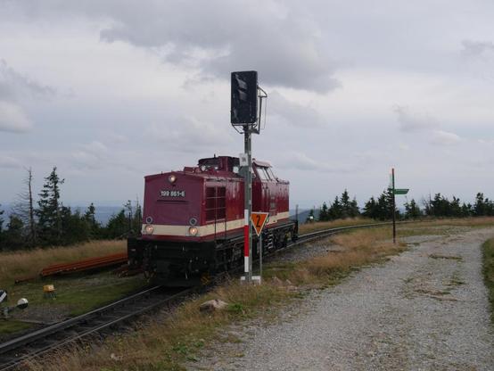 Das Foto zeigt eine rote Diesellokomitive der Baureihe 199 der Harzer Schmalspurbahnen auf dem Brocken beim rangieren am Ausfahrsignal 1N.
