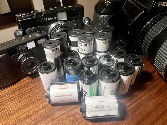 A pile of exposed 35mm and 120 film on a desk surrounded by cameras!